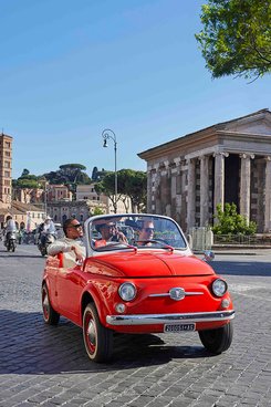 Drei Männer sitzen in einem roten Cabrio und fahren auf einer Straße in Rom. Verlinkung zu GetYourGuide Angeboten.